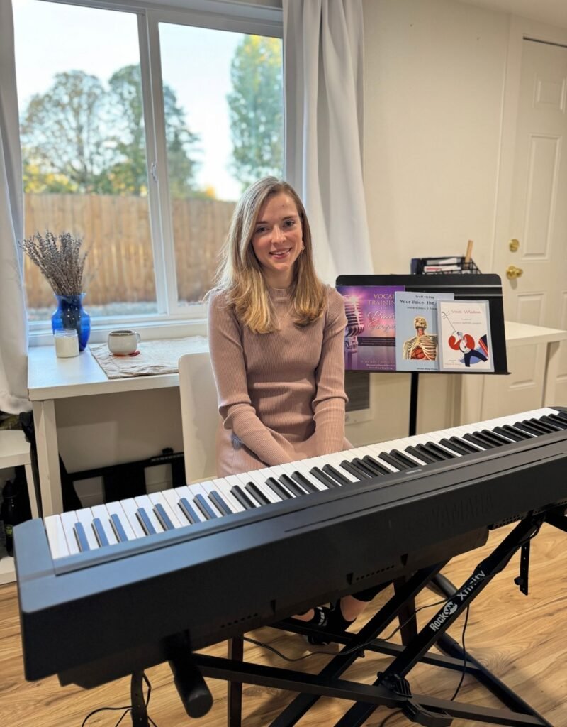 Amanda at her online teaching studio with piano and vocal health books at the ready.