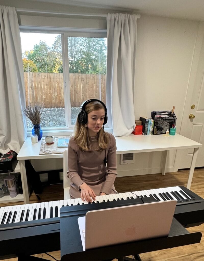 Image of Amanda teaching a student online with her laptop and piano and headphones.
